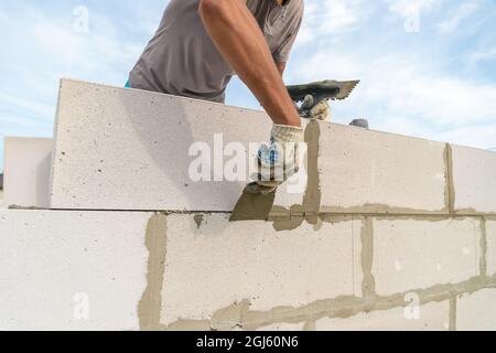 Worker wipes the seams with a spatula outside the house of blocks. Bricklayer worker laying white blocks of a future house in the open air. Stock Photo