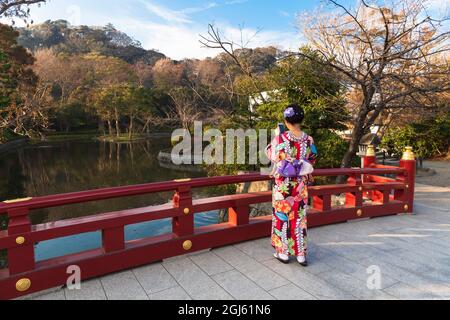 A Japanese women in kimono standing on a bridge overlooking a garden pond, taking a picture with her phone at the Tsurugaoka Hachimangu shrine. Stock Photo