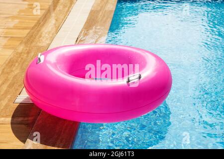 Pink Inflatable ring floating in swimming pool. Refreshing blue water. Summer travel hotel vacation - Image Stock Photo