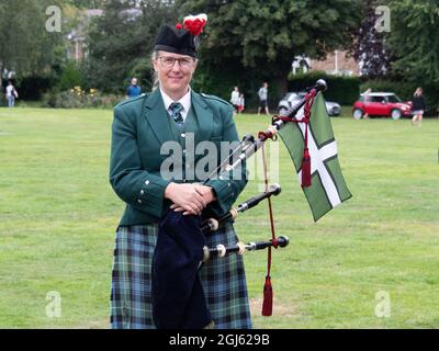 BIDEFORD, NORTH DEVON, ENGLAND - AUGUST 30 2021: Classic mini cars in The Legendary Grand Tour support Children's Hospice SW. Woman with bagpipes Stock Photo