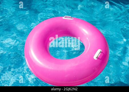 Pink Inflatable ring floating in swimming pool. Clear blue water, waves. Summer travel hotel vacation - Image Stock Photo