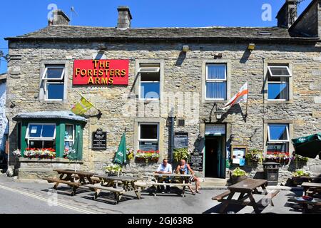 Stone walls of Foresters Arms Pub with restaurant & accommodation people sitting outside on a sunny summer blue sky day Grassington Yorkshire England Stock Photo