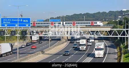 M25 motorway gantry signs railway bridge & Greater Anglia passenger train crossing above road traffic junction 28 for A12 Brentwood Essex England UK Stock Photo