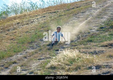 The boy comes down from the hill picking up dust Stock Photo