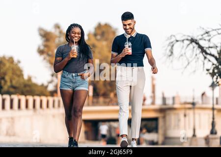 Two people of different ethnicities walking while drinking a shake outdoors Stock Photo