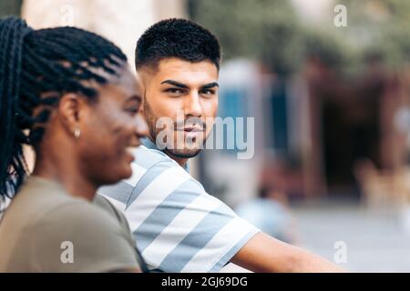 Young caucasian man facing the camera next to an afro woman outdoors Stock Photo