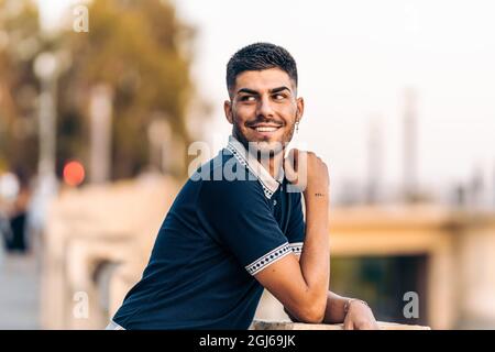 Man in modern clothes looking distracted while smiling in the street Stock Photo