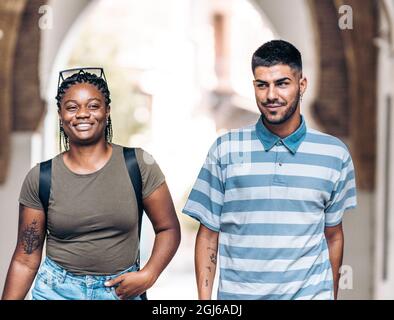 Two young people of different ethnicities smiling as they stroll through a city Stock Photo