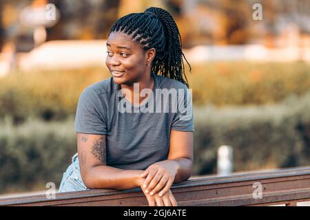 Distracted afro woman with summer clothes leaning on a rail in the street Stock Photo