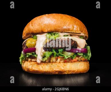 Craft burger is cooking on black background. Consist: red sauce salsa, lettuce, red onion, pickle, cheese, chilli green pepper, air bun and marbled me Stock Photo