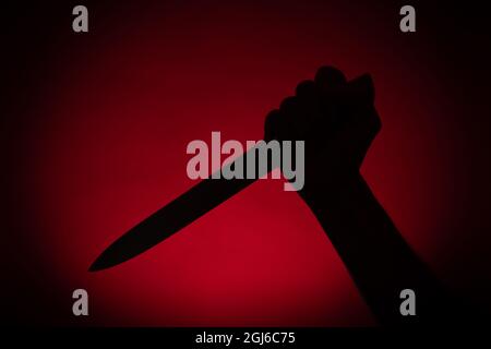 Hand with a knife silhouette in red background. Halloween and violence concept Stock Photo