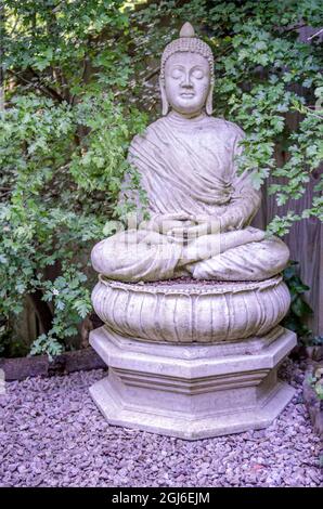 Buddah statue in crossed leg lotus meditation position on base in an English UK garden Stock Photo