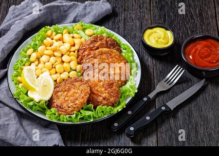 baked pork patties with browned cheese crust on a green lettuce lives with  lupine beans, ketchup and mustard on a plate Stock Photo