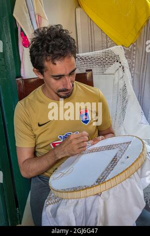 A young man in yellow shirt does embroidery for tourist articles in Trinidad, Cuba Stock Photo