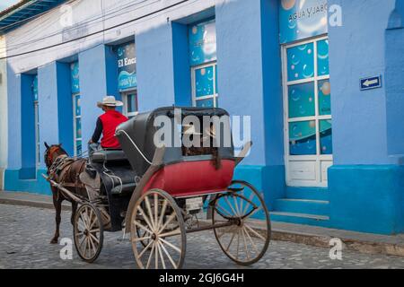 A cowboy drives a horse drawn carriage on cobblestone street in Trinidad, Cuba Stock Photo