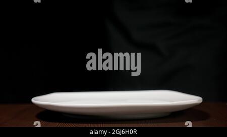 White plate of square shape. The dishes are on a black background on a brown table. Side view. Stock Photo