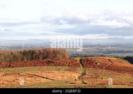 Large arching hill on horizon and forest. Wind turbine behind the forest communicating sustainable cities, then on the right, houses and a town. Stock Photo
