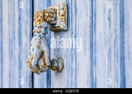 Europe, France, Dordogne, Hautefort. A rusted metal door knocker in the shape of a hand on a blue door in the town of Hautefort. Stock Photo