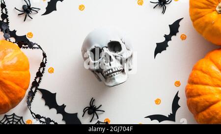 Halloween skull and decorations on white table top view. Flat lay pumpkins, bats, spiders, skull. Halloween greeting card. Stock Photo