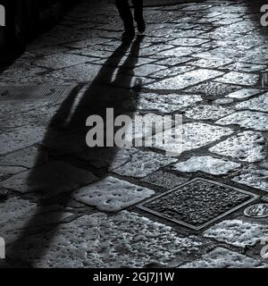 Shadow of a person walking on a cobblestone street. Stock Photo