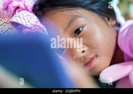 Asian girl lays happily watching cartoons on her smartphone in her bed at night. Stock Photo
