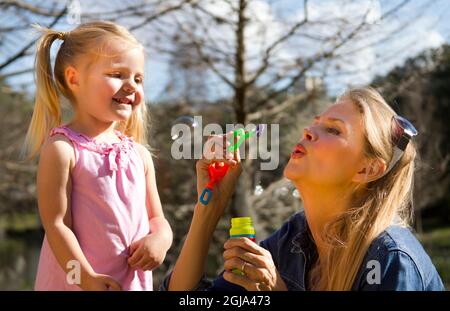 Mother and daughter blowing bubbles in park. Stock Photo