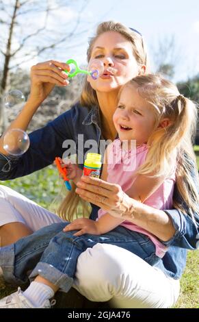 Mother and daughter blowing bubbles in park. Stock Photo