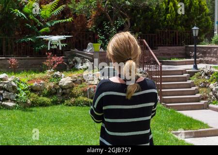 young woman flying drone in the garden of their house. Selective Focus remote control. Stock Photo