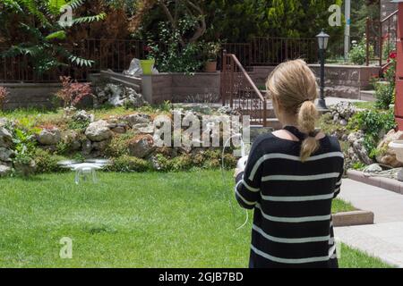 young woman flying drone in the garden of their house. Selective Focus remote control. Stock Photo