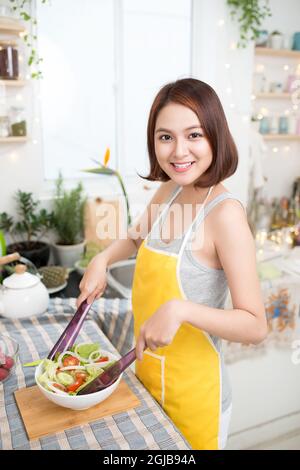 Young asian woman making salad in kitchen smiling and laughing happy at home. Stock Photo