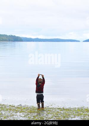 Alaska, Ketchikan, 2 year old boy throwing rocks in ocean. Stock Photo