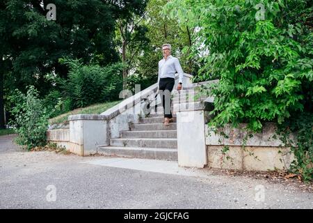 Businessman carrying folded e-scooter in hand down stairs. Moving by eco urban transport, modern city concept Stock Photo