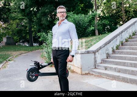 Businessman carrying folded e-scooter in hand down stairs. Moving by eco urban transport, modern city concept Stock Photo