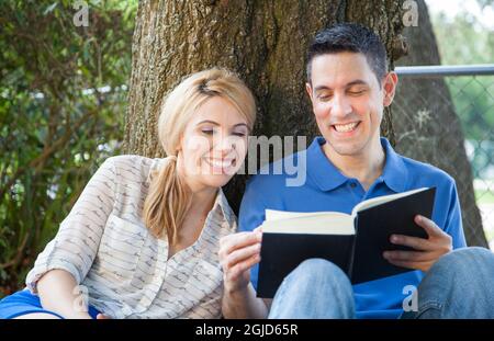 Young Hispanic man reading book in park in Florida (MR). Stock Photo