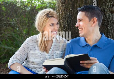 Young Hispanic man reading book in park in Florida (MR). Stock Photo