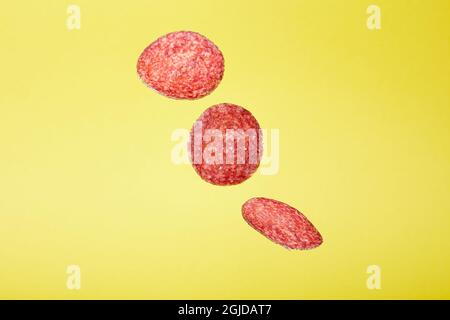 Closeup of falling salami slices isolated on a yellow background Stock Photo