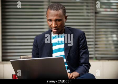 Image of a serious handsome young business man sitting near the business center working on the laptop. Stock Photo