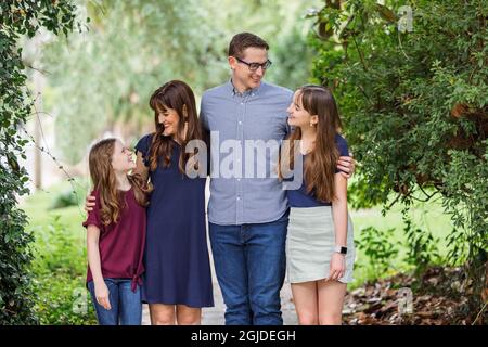 A family of a mother and father and two daughters standing on the sidewalk outside in the summer or fall Stock Photo