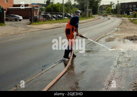 A worker washes the road with a hydrant. Hose with water jet. Washing away dirt from the road. Stock Photo