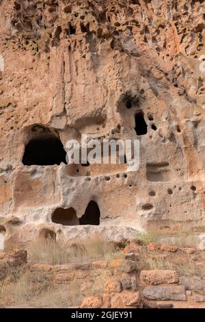 USA, New Mexico. Bandelier National Monument, Stone ruins below entrances to dwellings carved into soft, volcanic rock called tuff in Frijoles Canyon. Stock Photo