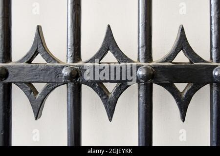 Old forged lattice with round rods, rivets and curly elements. Grate is painted with a black protective varnish and placed on a gray background. Close Stock Photo