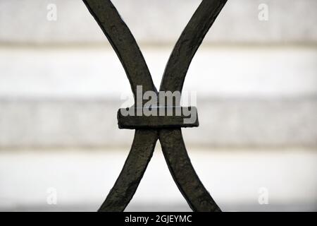 Fragment of an old wrought-iron fence, painted with black paint on the background of a striped blurred wall. In the form of the letter X. Close-up. Se Stock Photo