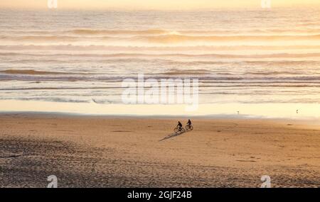 USA, Oregon, Cape Arch with two riding bikes on the beach in the evening light Stock Photo