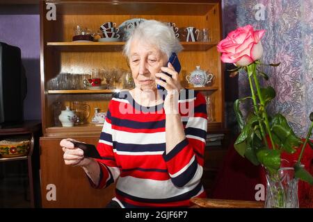 Serious senior woman with face mask making reservation online from home and paying with credit card. Active elderly people interacting with new technologies during quarantine Stock Photo