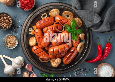 Delicious fried sausages, spices, garlic and onions on a dark background. Stock Photo