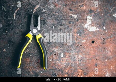 Yellow pliers on wooden workbench. New pliers with yellow and black grip isolated on wooden background. Top view. Repair or building tools. Stock Photo