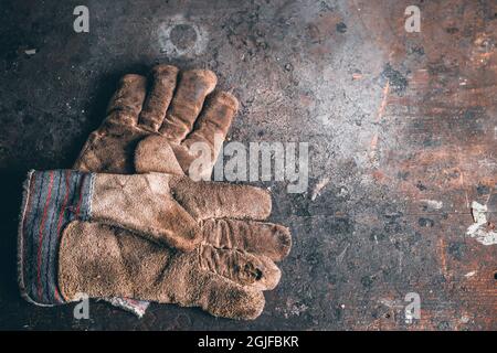 A pair of protection gloves. Old leather gloves on wooden table. Working gloves on wood workbench. A dirty and well-worn pair leather work gloves. Stock Photo
