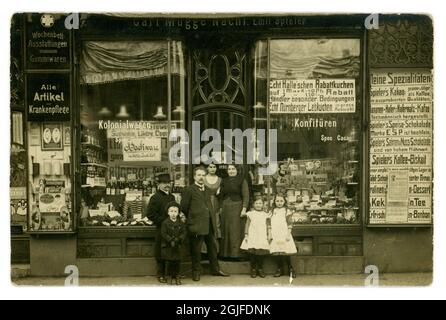 German family and proprietors outside a large grocery shop front, lots of brands, cakes, tea and coffee, special offers posters, well-dressed men, the proprietors perhaps - the  shop sign reads Carl Mugge Nacht Emil Spieler  circa 1914, Germany Stock Photo