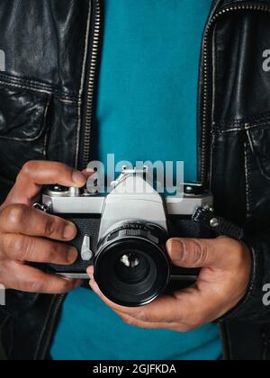 Ethnic person wearing a leather jacket and holding a vintage analogue SLR film camera Stock Photo