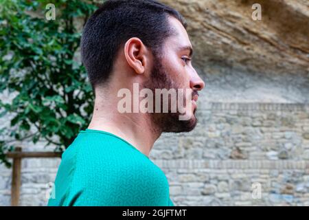 Young Caucasian bearded man wearing a green shirt and walking in a park Stock Photo